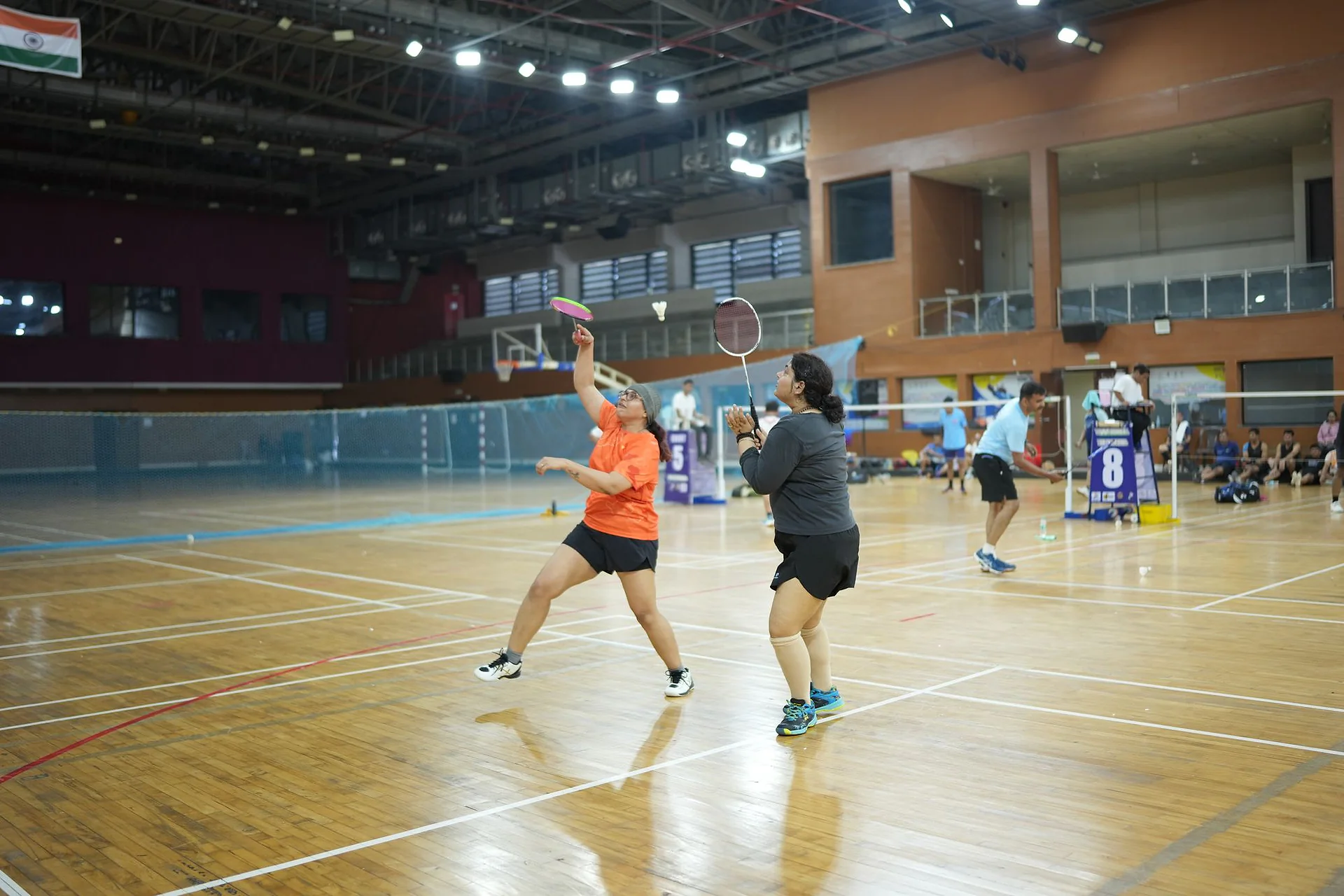 Doctors playing doubles badminton on a wooden indoor court