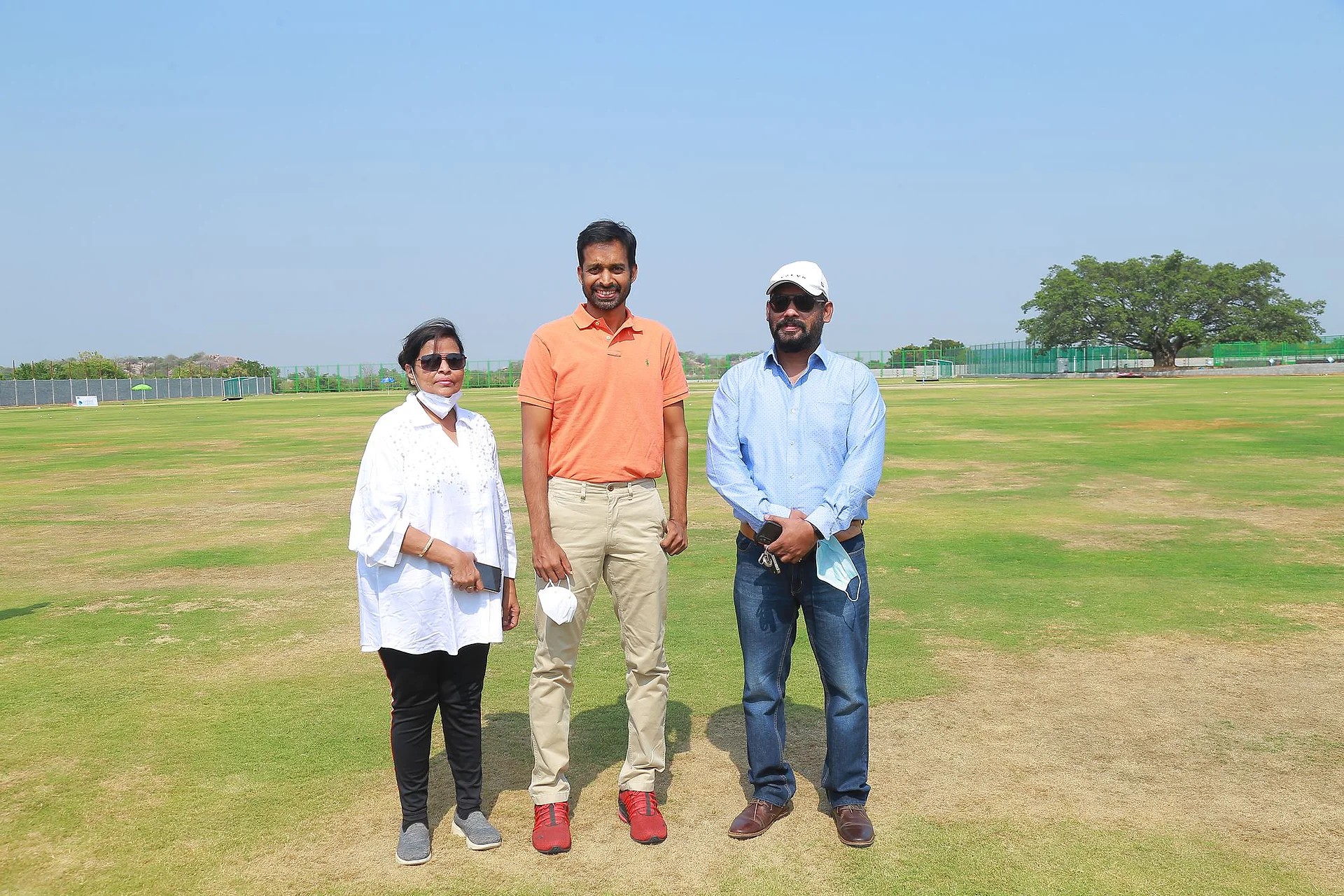 Three people standing together on the cricket ground before play