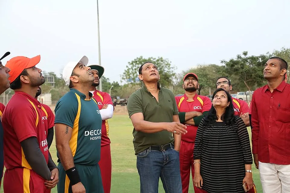 Players in red and green kit gathered on the ground with guests at a Doctors Cricket League match