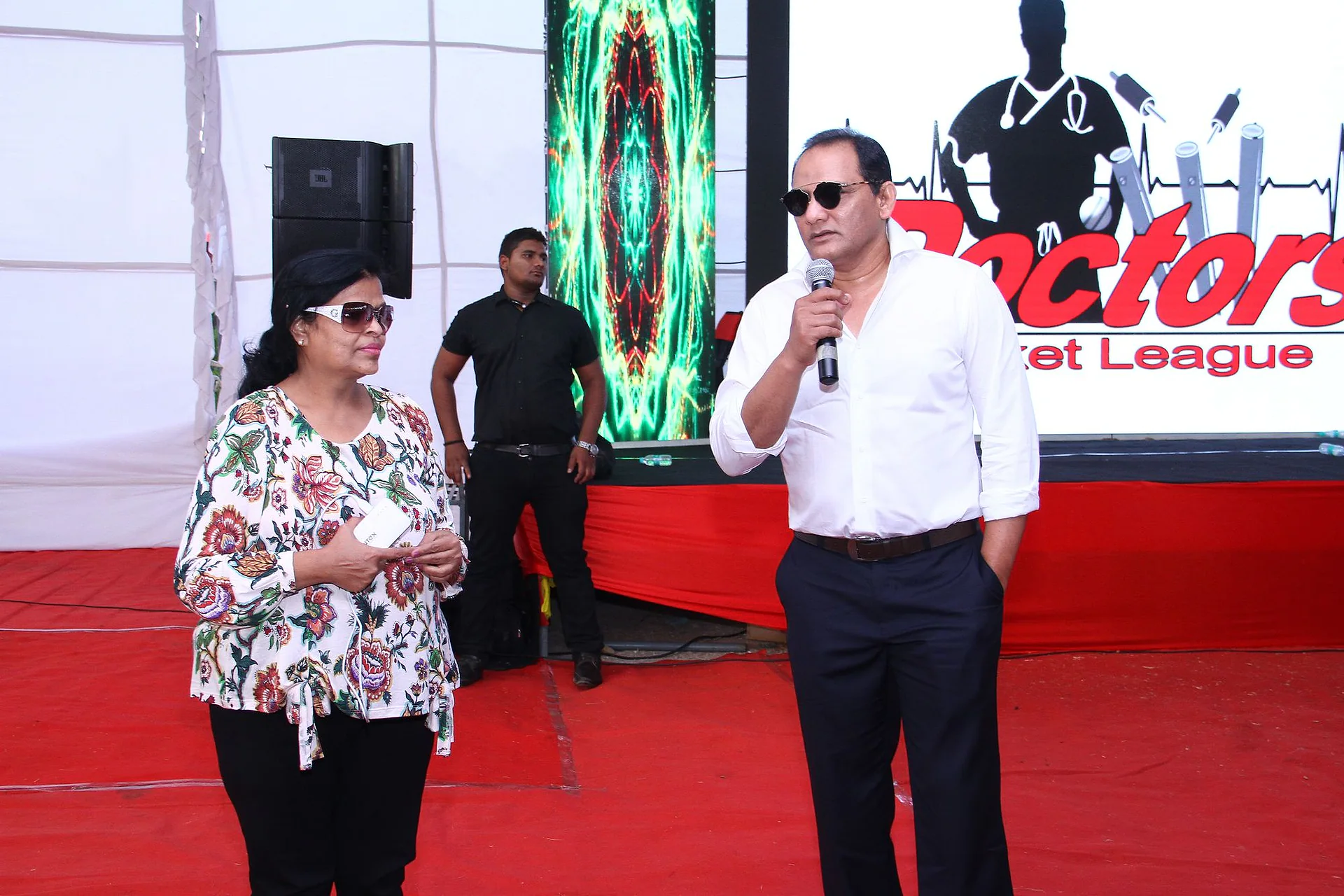 Hosts speaking on a red-carpeted stage at a Doctors Cricket League ceremony