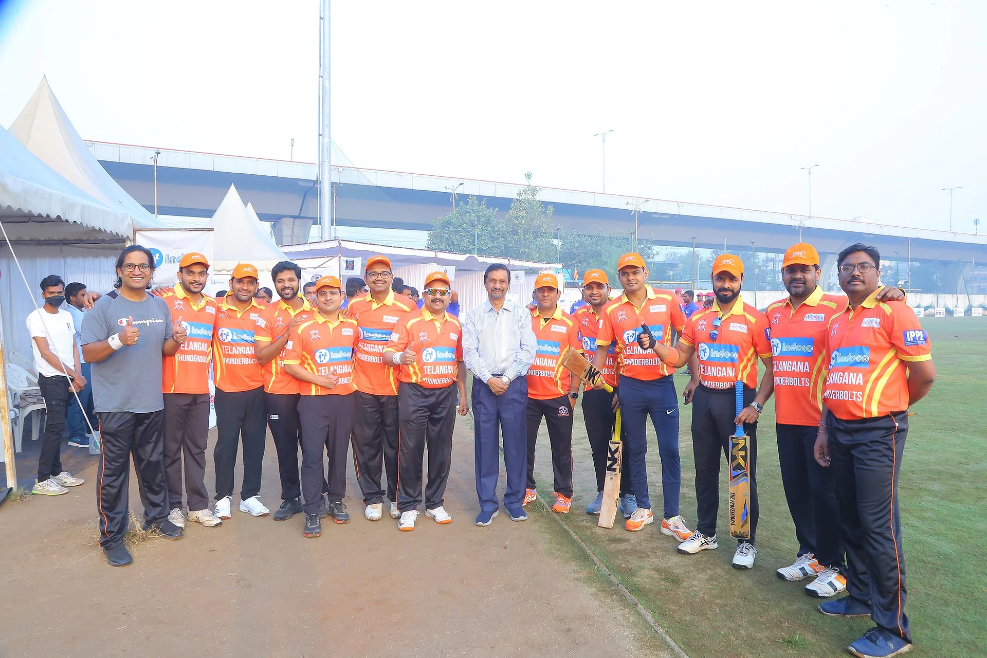 A pediatricians' cricket team in orange Telangana Thunderbolts jerseys lined up on the outfield