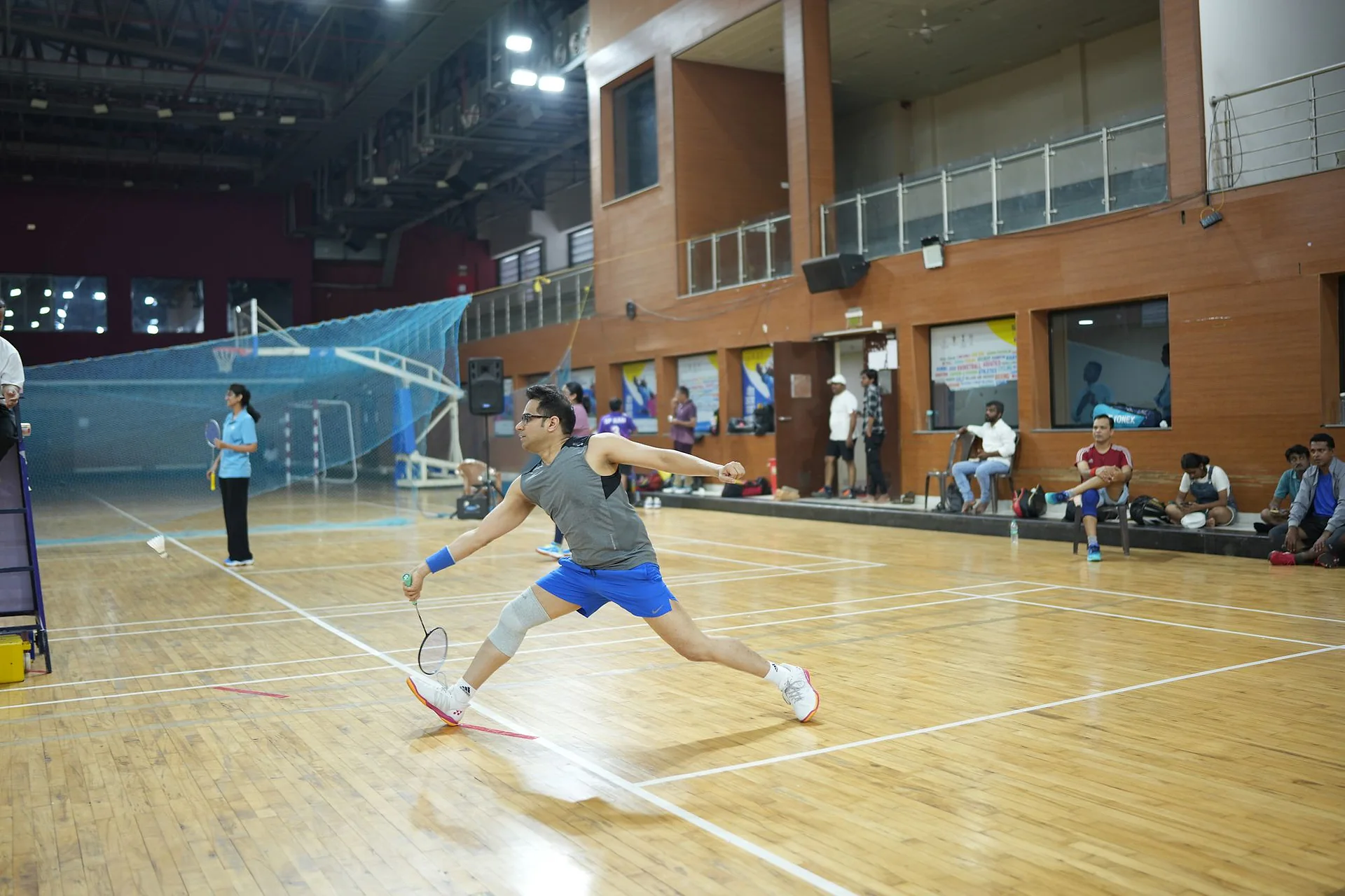 A player stretching for a return on a wooden court at the National Doctors Badminton Championship