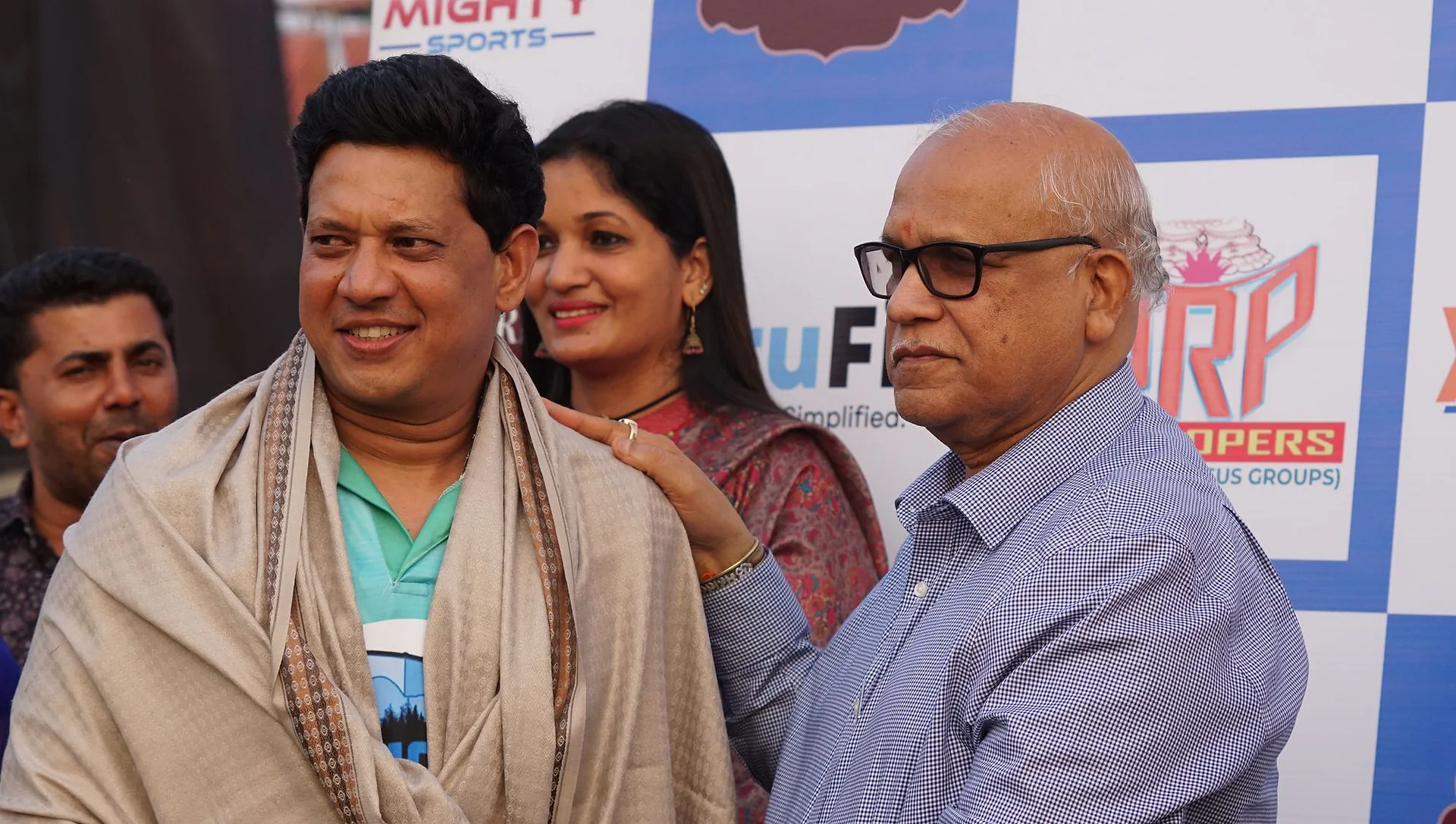 Guests being felicitated with shawls in front of the Mighty Sports banner